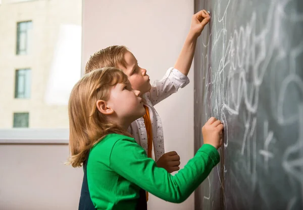Little kids writing on blackboard. Happy kids count and draw numbers. Back to school.