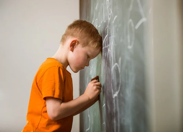 一个脑袋在黑板上的可悲的孩子 很难理解 回学校去 — 图库照片