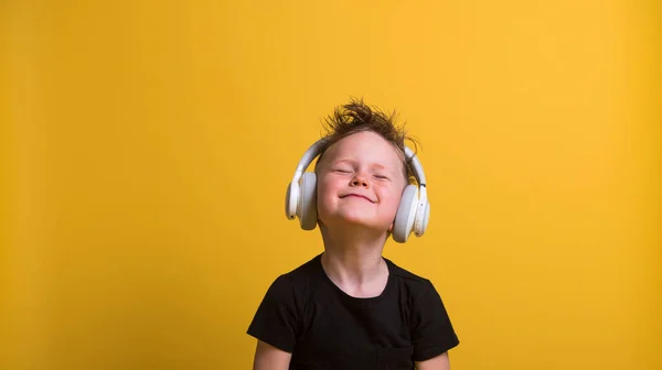 Kulaklıklı komik sarışın çocuk. Mutlu gülümseyen çocuk müzik dinliyor.
