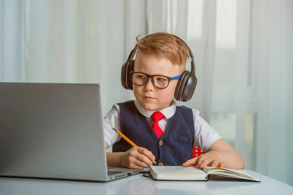 Barn som använder en bärbar dator medan du gör läxor på nätet på bärbar dator. Pupil i hörlurar. Lär engelska. — Stockfoto