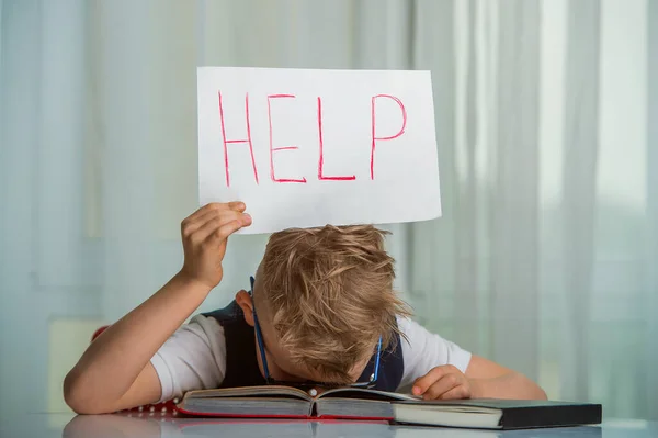 Niño durmiendo con un libro de texto sobre su cabeza y sosteniendo un cartel con la palabra Ayuda —  Fotos de Stock