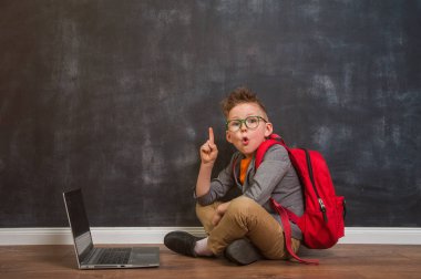 Dizüstü bilgisayarı olan küçük bir çocuğun portresi ahşap zeminde parmak yukarıda oturuyor. Okula geri dön..