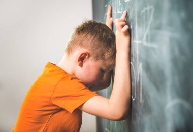Tahtanın yanında bir sürü sorusu olan bir çocuk. Eğitmesi zor. Çocuk ellerini tahtaya koydu.
