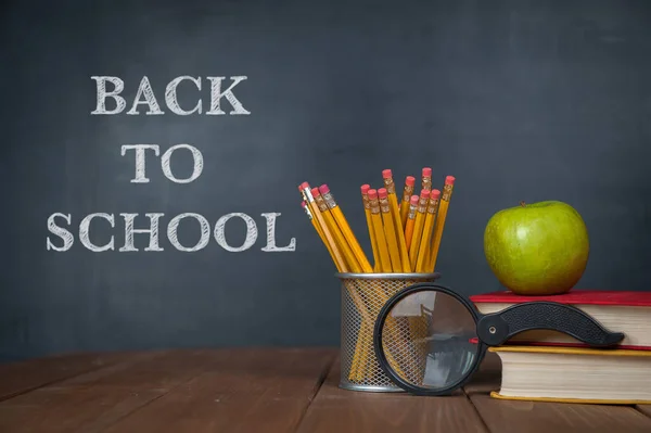 stock image Back to school. Desk, alarm clock, apple, pencils and school books against blackboard with back to school on background.