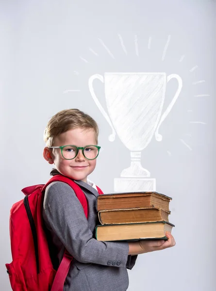 Portrait of child with stack of books and win cup. Kid with books in class. Success, idea and win concept. Back to school. Smart pupil in glasses.