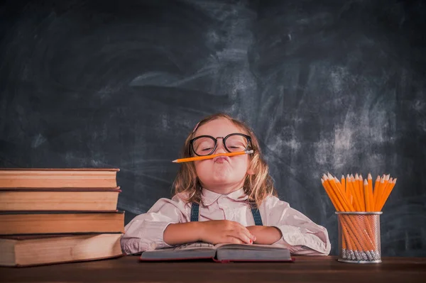 De vuelta a la escuela. Chica hipster divertido en la sala de la escuela divirtiéndose con lápiz. Montón de libros en el escritorio. Filtro Instagram . — Foto de Stock