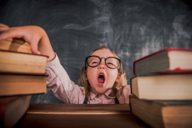 Okula dönelim. Gözlüklü çocuk elinde kitaplarla masada oturuyor. Gözbebeği esniyor. Çocuk ev ödevi yaparken sıkıldı. Küçük öğrenci bağırıyor. Stres.
