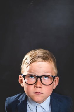 Düşünen çocuk. Akıllı bir okul çocuğunun portresi. Başparmağı tahtada boş ve kameraya bakıyor. Üniformalı mutlu çocuk. Okula geri dön. Sonbaharın ilk günü