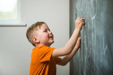 Tahtaya yazı yazan çocuk. Okula dönelim. Sınıfta elinde tebeşirle dolaşan bir çocuk. Düşünen öğrenci. Dahi.