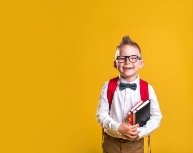 Gülen çocuk okula gitmeye hazır. Sarı arka planda mutlu bir çocuk. Eğitim kavramı.