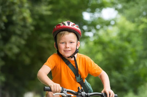 Porträt eines netten Jungen auf dem Fahrrad. Kind mit Schutzhelm und orangefarbenem Hemd spielt draußen im Park. Sport- und Gesundheitskonzept. Schulkind im Fahrrad — Stockfoto