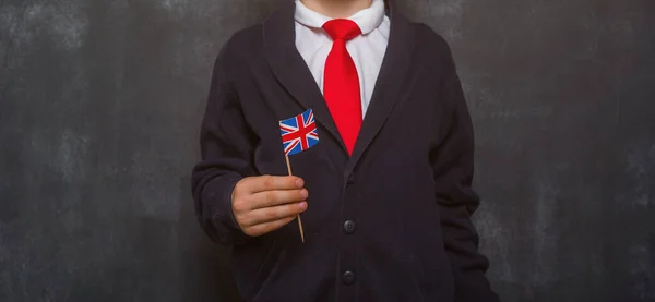 Kid in uniform holding a flag of United Kingdom and book in hands. Great Britain flag. British flag. Education and learn English. International language school concept. Blackboard