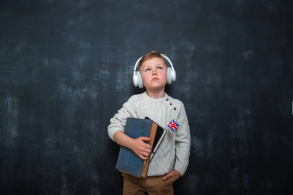 Kid in uniform and headphones holding a flag of United Kingdom and book in hands. Great Britain flag. British flag. Education and learn English. International language school concept. Leader