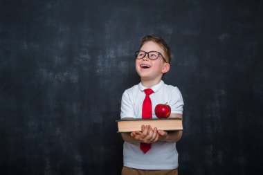 Sevimli çocuk Whit kitapları ve elma ellerinde. Okula dönelim. Eğitim. Arkaplanda karatahta. Üniformalı çocuk. Mutlu çocuk