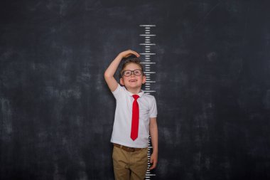 Küçük çocuk kendini ölçüyor. Okullu çocuk boyunu karatahta ölçüsünde ölçüyor. Okula dönelim. Üniformalı öğrenci.