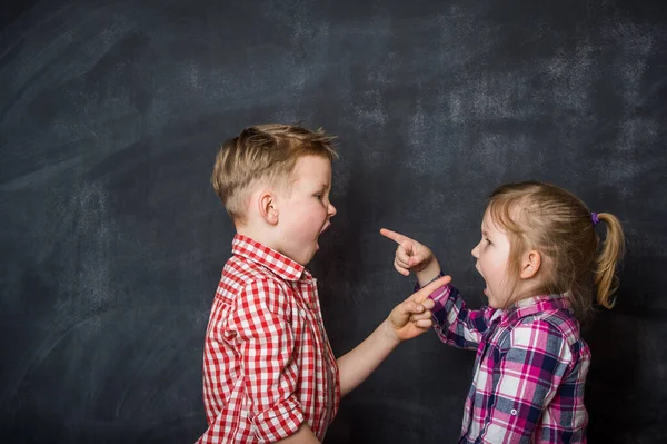 男孩和女孩互相指指点点 愤怒的孩子 孩子们在黑板的背景下互相喊叫 愤怒的孩子 — 图库照片