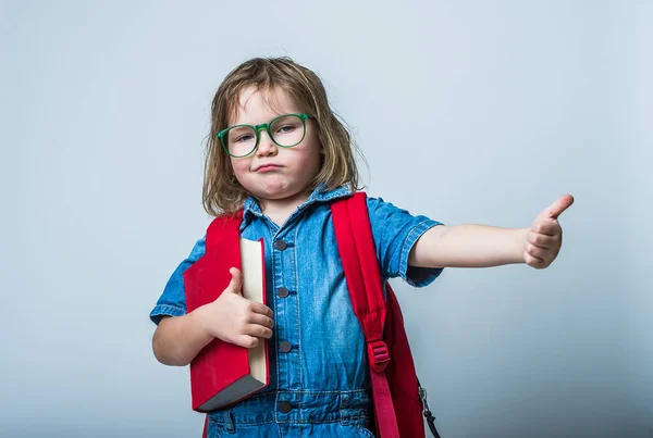 一个戴着眼镜抱着一本书的快乐小女孩的画像 背着背包笑着指指点点的孩子 — 图库照片