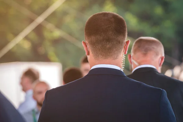 Protection and guard service. bodyguard man with earphone and black eyeglasses and business suit wearing a mask during the Covid-19 outbreak, during a public visit of a dignitary. crowd.