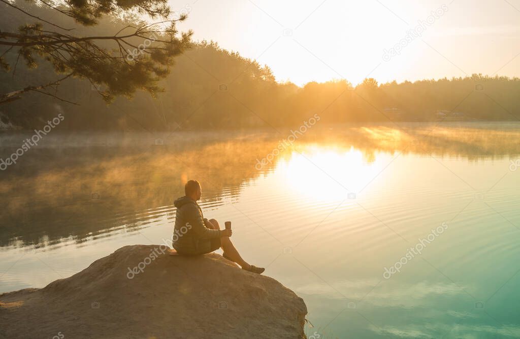 Man sitting on a lake on top of a mountain at sunrise. inspiration concept, enjoy life. Businessman with hands up. Winner. Champion. Leader.