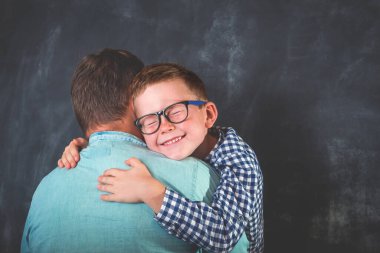 Küçük çocuk babasına sarılıyor. Gözlüklü şirin çocuk babasına sarılıyor. Oğul babasına sarılıyor. Mutlu aile zamanları. Sevgi. Baba oğul duygusal bağ.