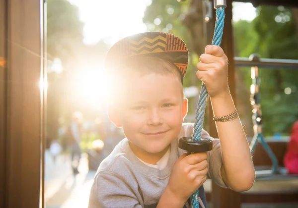 滑稽的微笑的孩子在户外玩耍。在室外操场上，一个高加索小男孩手搭在猴栏上做运动。阳光下的小男孩 — 图库照片