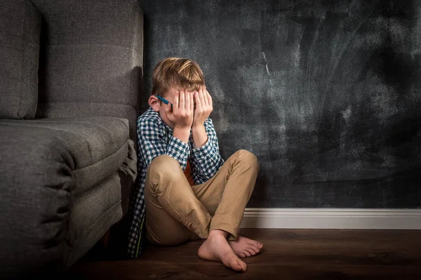 Alone sad and depressed kid boy sitting near the wall. Stressed child. Domestic Family violence and aggression concept violence. concept for bullying, depression stress or frustration