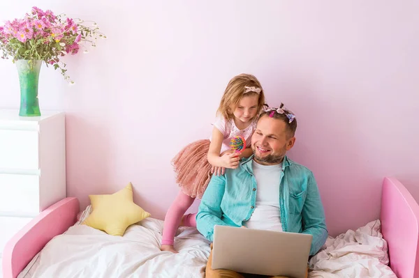 Work from home. Stress to work with family around. Parent at home office because of covid 19. Fathers day with daughter in pink room. Cute girl putting on make up on her father
