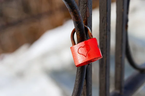 Red love padlock attached to steel fence. Rusty lock with heart