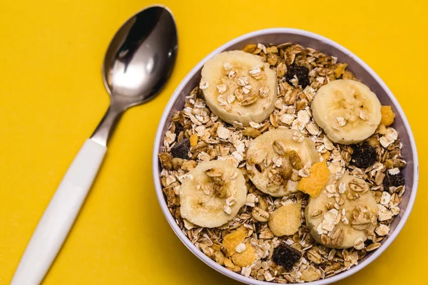 A white bowl with banana, oatmeal and cereal, with yellow background. Perfect nutrition for a healthy diet or breakfast.