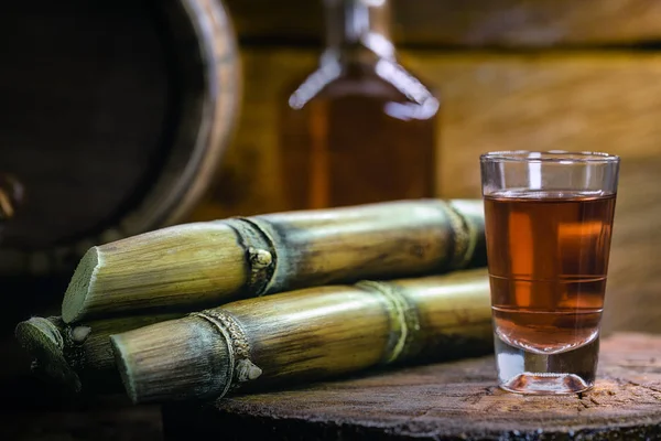 Shot glasses of Brazilian gold cachaca with sugar and sugarcane isolated on rustic wooden background — Stock Photo, Image