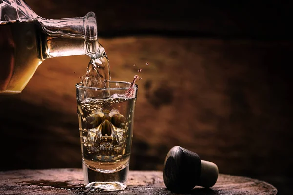 İçecek şişe ve cam alkol içeriği ile. Camda yarı saydam kafatası görüntüsü. Alkolizm, bağımlılık veya zehir kavramı.