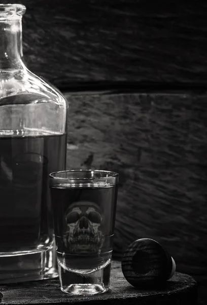 Питьевая бутылка и стекло с содержанием алкоголя. Изображение полупрозрачного черепа в стекле. Алкоголизм, зависимость или яд . — стоковое фото