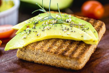 Biyolojik mayayla yapılan kızarmış vejetaryen ekmeğin üzerinde dilimlenmiş avokado, arka planda ise kırsal bir masada avokado. Hayvan unsurları olmayan vejetaryen yemekleri.