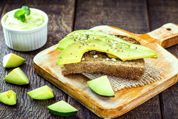 sliced avocado on toasted vegan bread made with biological yeast, with avocado in the background on a rustic table. Vegan food, without animal elements