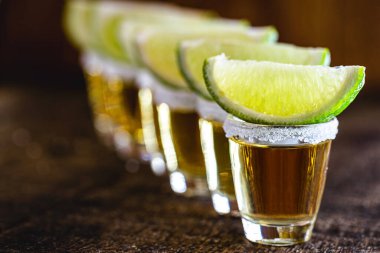 Sıraya dizilmiş birkaç bardak tekila, damıtılmış alkol, limon, tuz ve mavi agave 'den yapılmış Meksika kültürü. Uluslararası tekila günü. metin için kopyala.