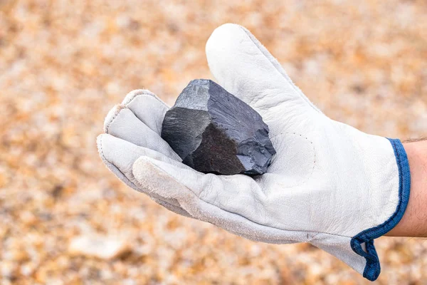 miner hand holding iron stone, metallic iron pyrite, steel, used in heavy industrial production. Mineral extraction concept.