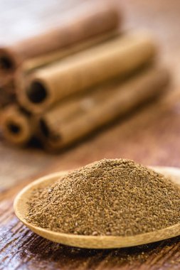Bir kaşık pudra tarçın, arka planda tarçın çubukları, spot odak. Mutfak malzemeleri tatlı ya da tuzlu olarak kullanılır..