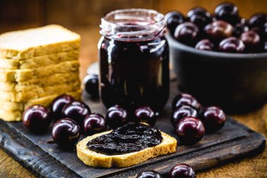 Kırsal ahşap masada üzüm reçelli tost. Jabuticaba, egzotik Brezilya meyvesi, yemek pişirmede tatlı olarak kullanılır..