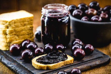 toast with grape jam, on rustic wooden table. Jabuticaba, exotic Brazilian fruit, used in cooking, as a sweet. clipart