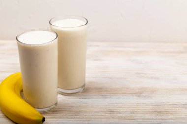 Muzlu milkshake. Serinletici muzlu smoothie, olgun muz eşliğinde iki bardakta servis edilir, kırsal ahşap masaya yerleştirilir, canlı ve sağlıklı bir içecek sahnesi yaratır. Muzlu smoothie.