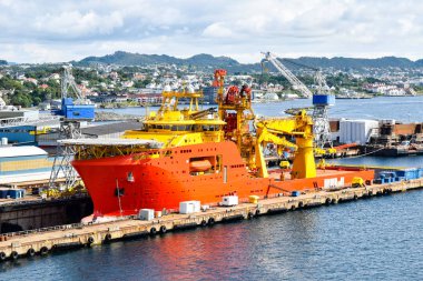 A large orange and yellow colored Offshore Construction Vessel (OCV) is in a dry dock of a shipyard and is being repaired clipart