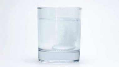 Fışkırtan aspirin beyaz arka planda bir bardak suda erir..