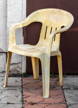 Arka bahçedeki duvarın yanında eski sarı bir plastik sandalye duruyor..