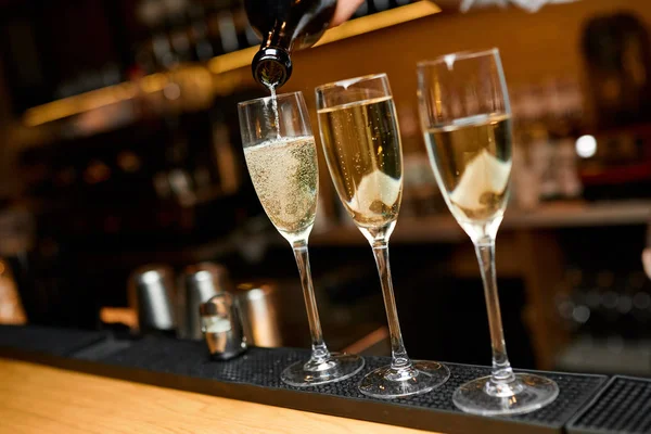 Champagne giet uit de fles in het glas met twee glazen in de buurt — Stockfoto