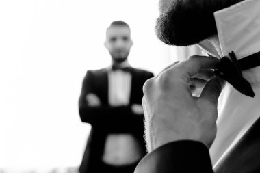 sakallı bir adam arkadaşı izlerken bir kravat doğrular