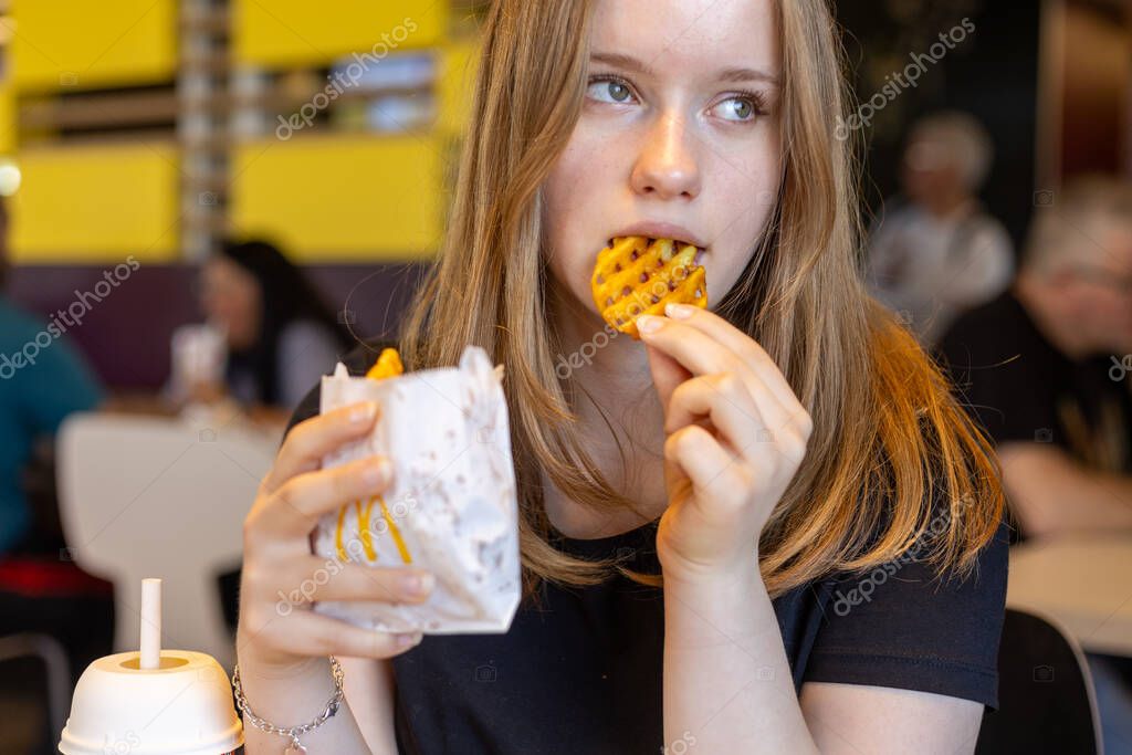 Kerpen, Germany - August, 9, 2025: Young woman eating waffle fries at McDonalds restaurant