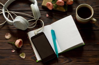 Smartphone, kulaklık ve açık defter ile sayfaları sonraki kahve ahşap tablo için boş. Üst görüntülemek düz yatıyordu arka plan.