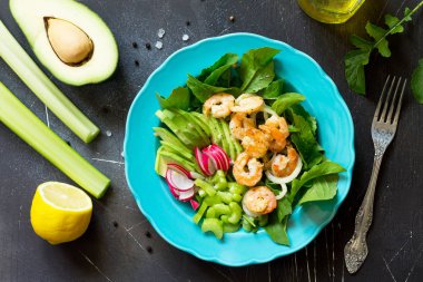 Izgara karides, rucola, turp, avokado, kereviz ve salata sosu karanlık arduvaz arka plan üzerinde sağlıklı sebze salatası. Diyet menüsü. Üst görüntülemek düz yatıyordu arka plan.