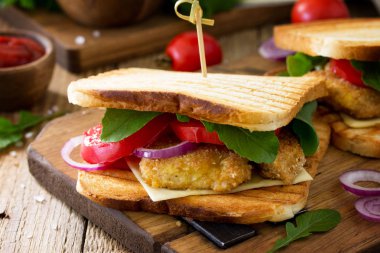 Club sandviç domates, peynir, kızarmış tavuk nuggets ve roka ile. Lezzetli taze ev yapımı club sandviç ile tavuk ahşap mutfak masasında. Fast food.