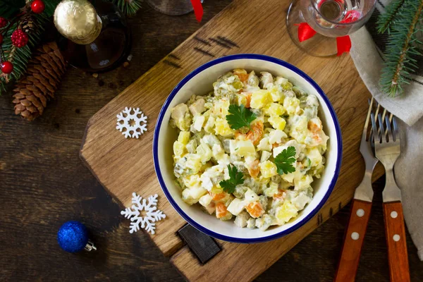 Winter holiday salad. Russian traditional salad Olivier with vegetables and chicken on wooden table. Traditional Russian cuisine. Top view flat lay background. Copy space.